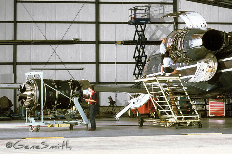 Expert technicians inspect and maintain Rolls Royce jet engines in massive jet hanger.