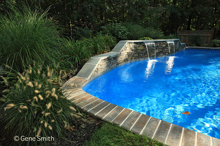 Pretty waterfal cascades into secluded swimming pool at edge of forrest.