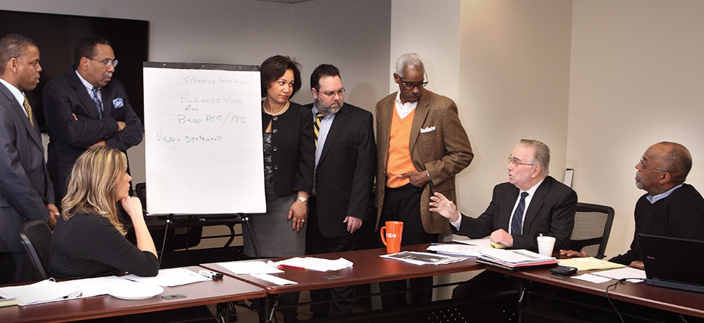 Diverse group of eight executives meet in conference room.