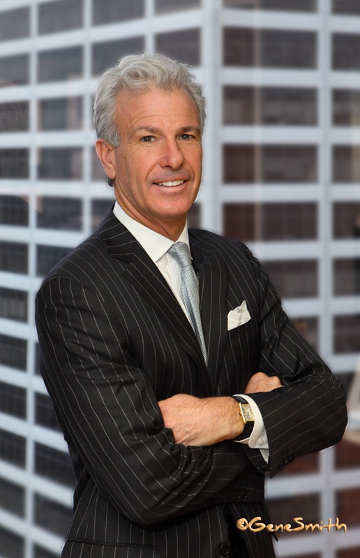 Executive attorney photographed in his office in urban setting with skyscraper in background through office window. This well groomed professional has striped suit silk tie and gold tank style watch.